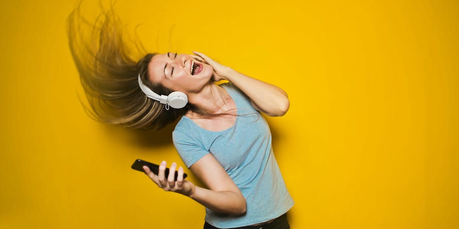 Een jonge vrouw die een koptelefoon draagt en naar muziek luistert op een gele achtergrond.