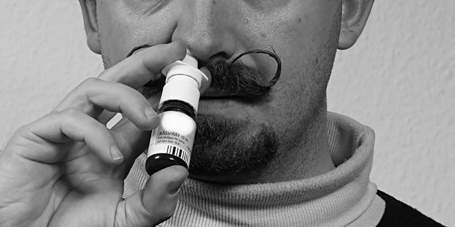 Zwart-wit foto van een man met een snor die neusspray spuit in zijn neus.