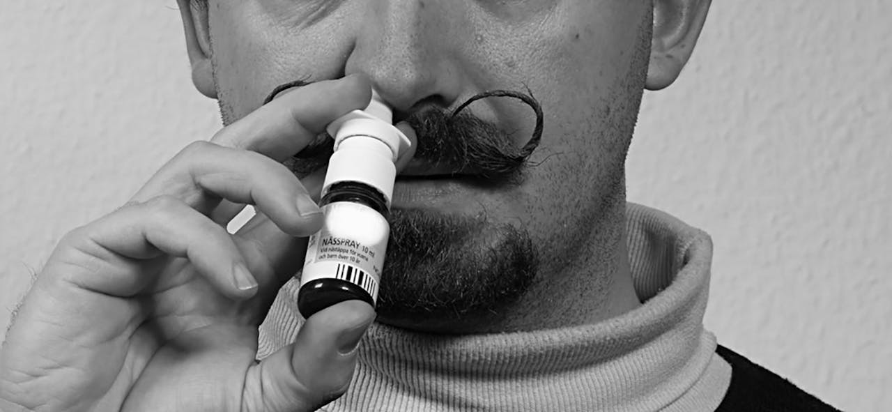 Zwart-wit foto van een man met een snor die neusspray spuit in zijn neus.
