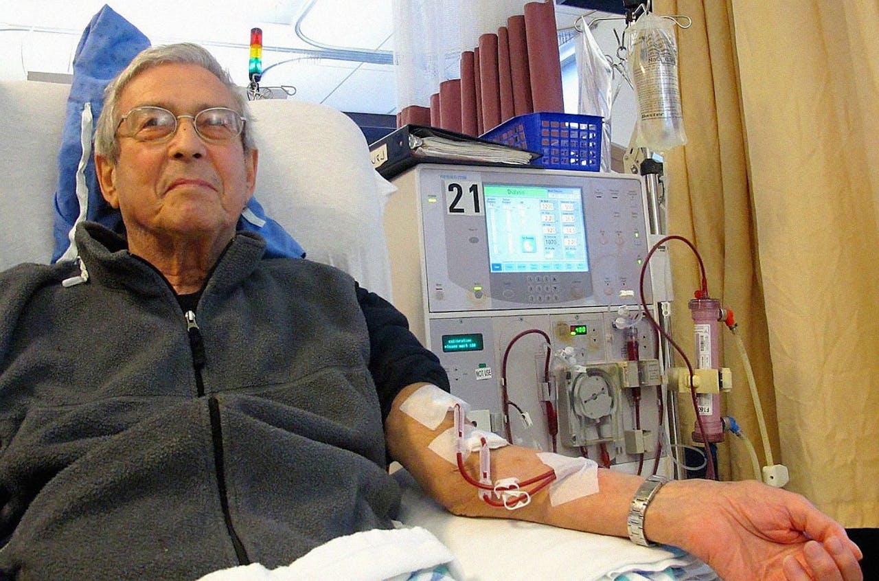 Een man zit in een ziekenhuisbed aan de nierdialyse.