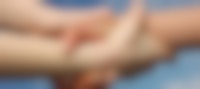 Een close-up van twee mensen die met hun hand elkaars pols vasthouden. Op de achtergrond is een blauwe lucht te zien.