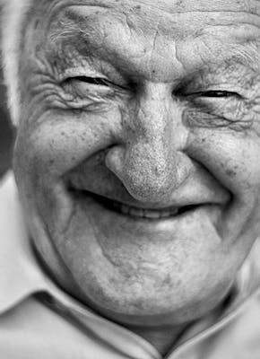 Een zwart-witfoto van een oudere man die lacht.