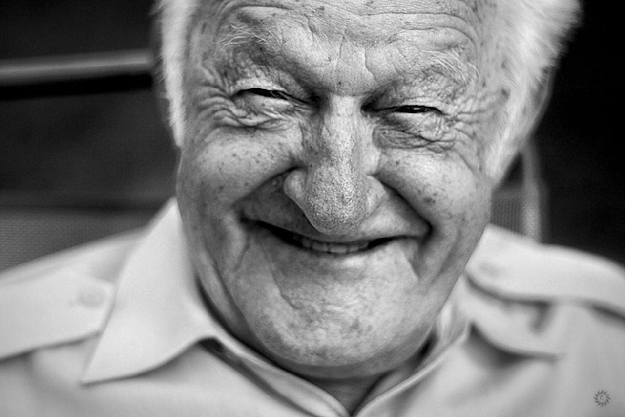 Een zwart-witfoto van een oudere man die lacht.