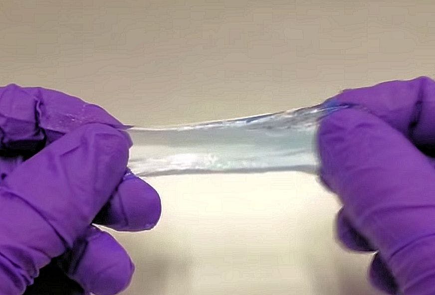 Een persoon die paarse handschoenen draagt, houdt een stuk gel vast.