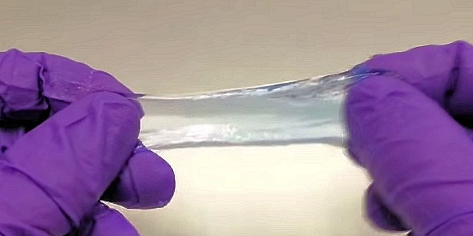 Een persoon die paarse handschoenen draagt, houdt een stuk gel vast.