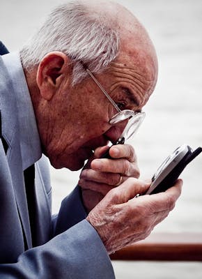 Een oudere man kijkt naar zijn mobiele telefoon met een vergrootglas in zijn hand.
