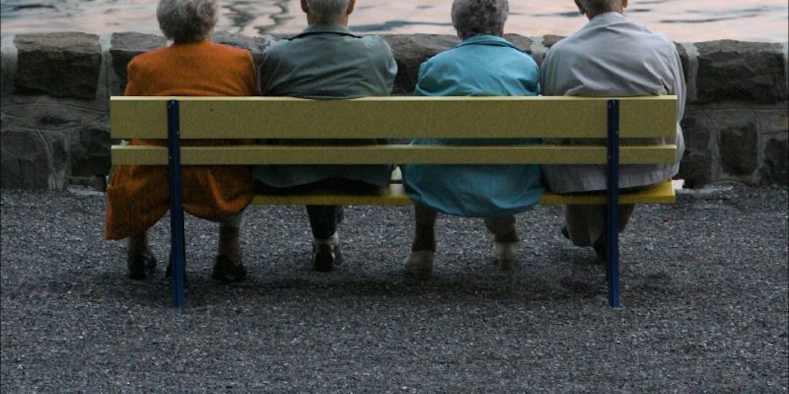 Een groep ouderen zit op een bankje voor een meer.
