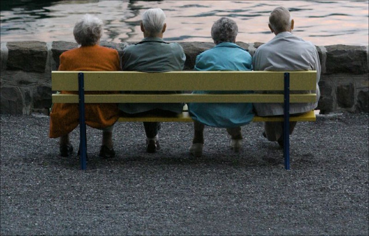 Een groep ouderen zit op een bankje voor een meer.