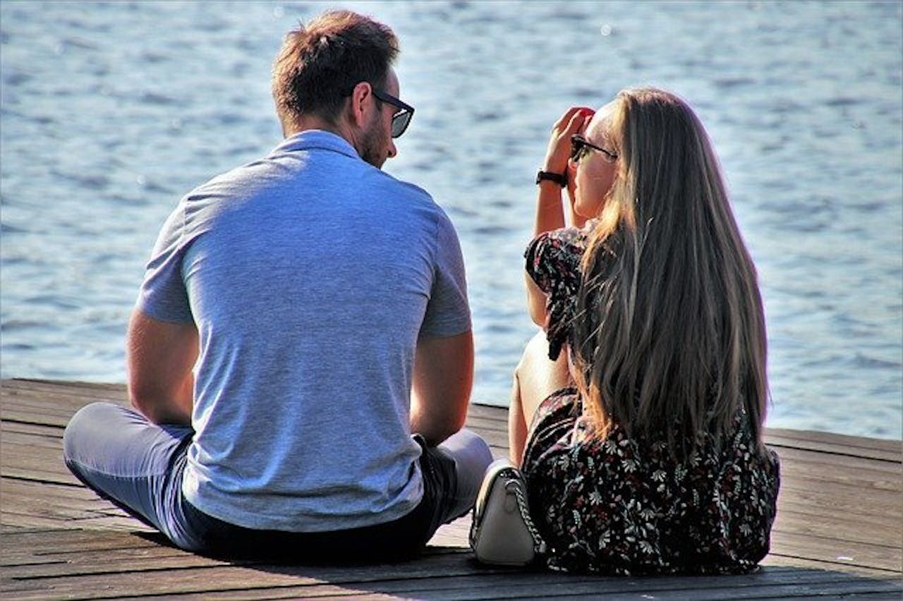 Een man en een vrouw zitten op een kade en kijken naar het water.
