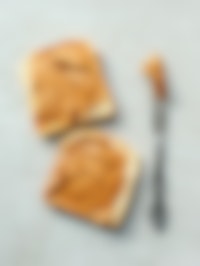 Twee witte boterhammen met pindakaas van boven gezien. Naast de boterhammen ligt een mes met daarop pindakaas.