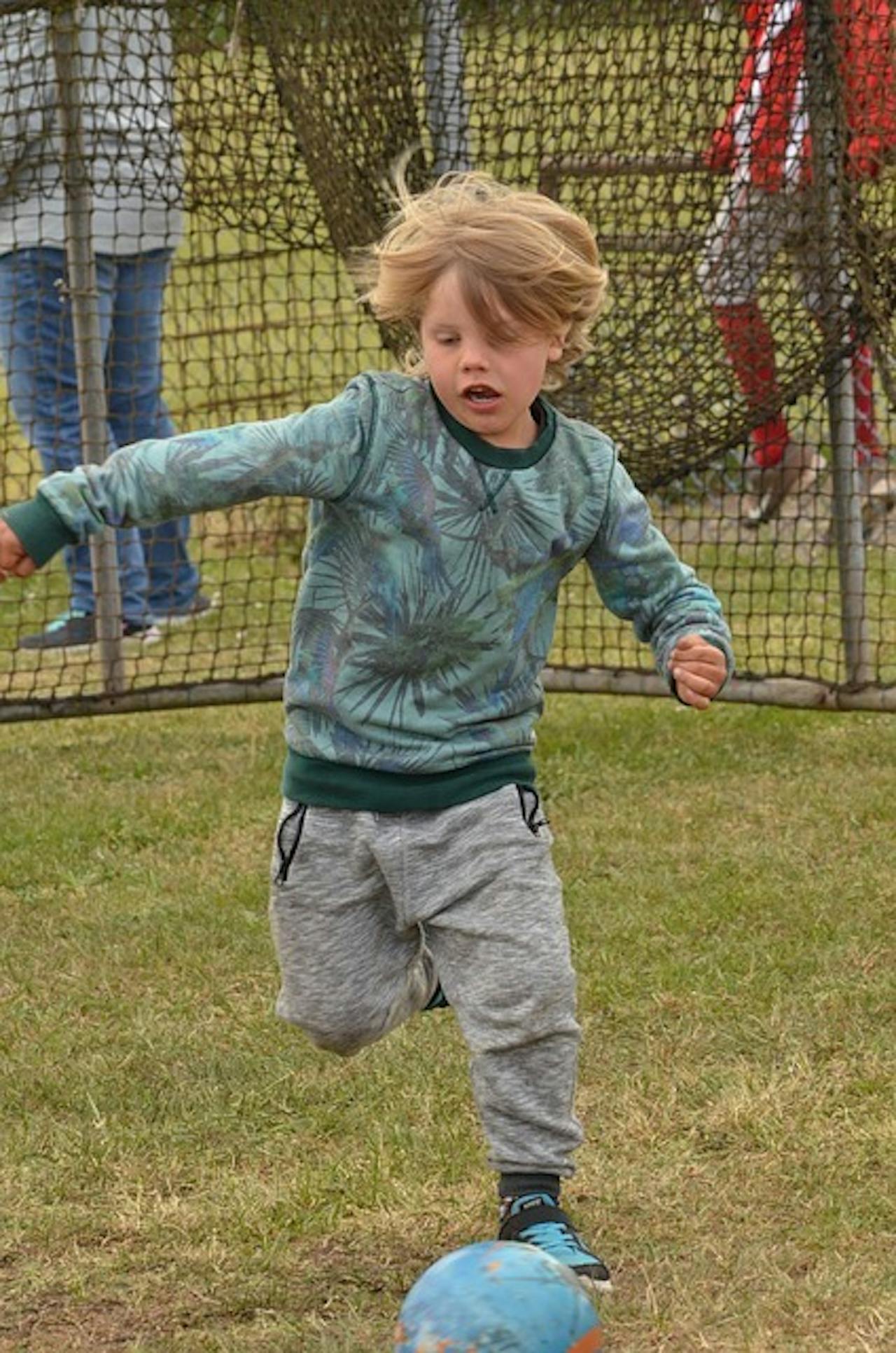 Een jonge jongen die een voetbal in een veld schopt. Achter hem zien we het doel.