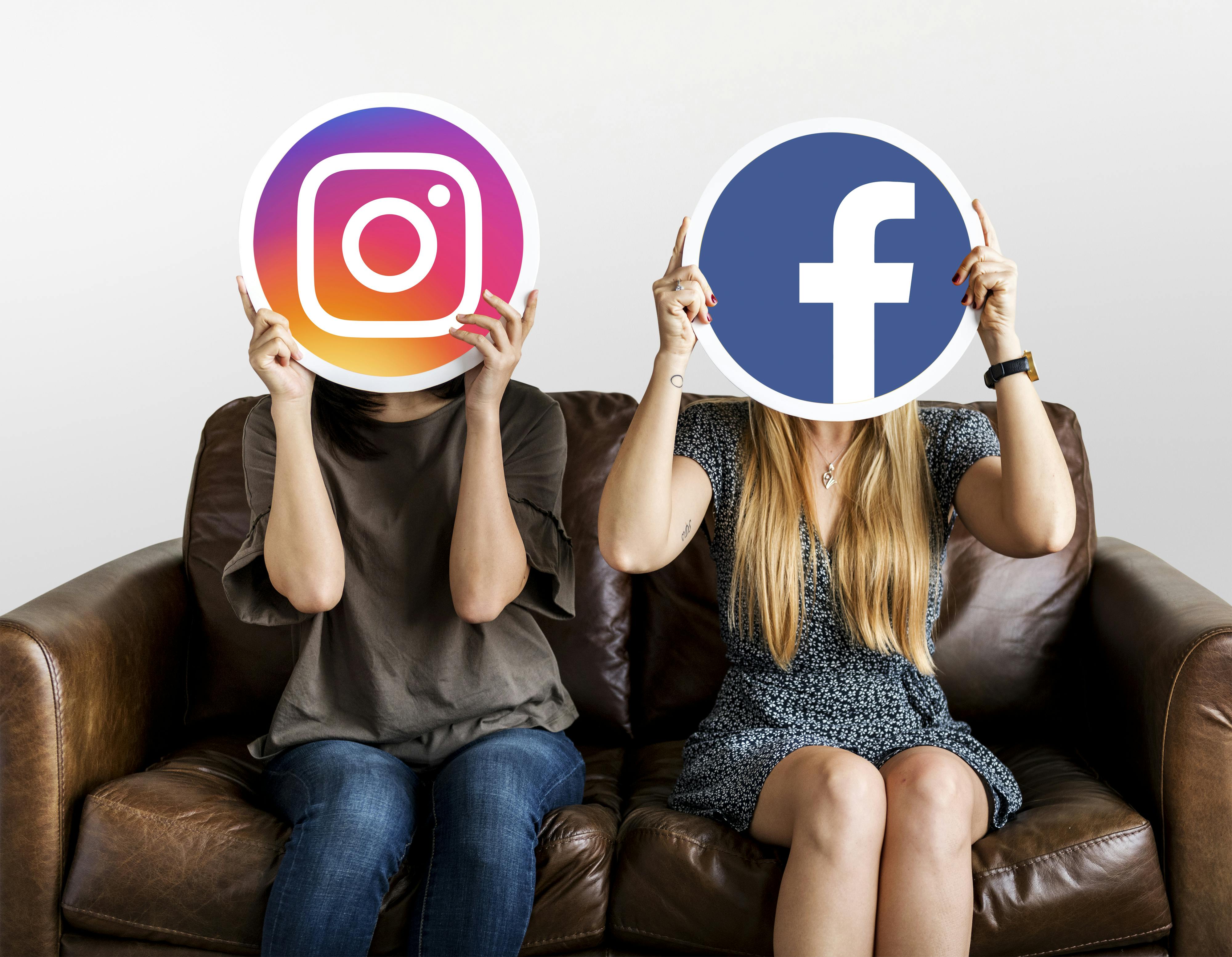 Twee mensen zitten op een bruine bank. De een houdt het icoon van Instagram voor het hoofd, de ander dat van Facebook.