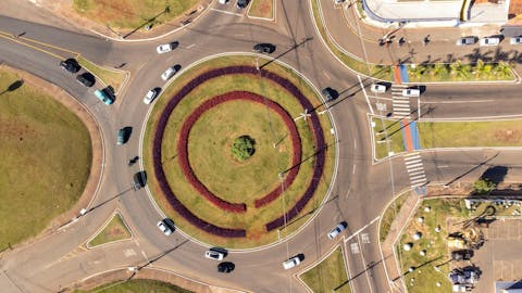 Als je met de auto een rotonde oprijdt, kun je maar op één punt in conflict komen met een andere auto. Bij elke ‘arm’ van de rotonde is er dus telkens maar één ander voertuig waar je op hoeft te letten. Luchtfoto van een verkeersrotonde met autoverkeer, van bovenaf genomen
