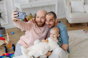 Twee mannen en een baby maken een selfie in een woonkamer.
