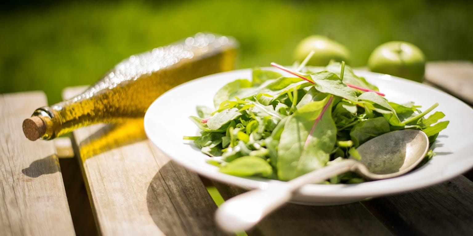 Een bord spinaziesalade op een houten tafel.