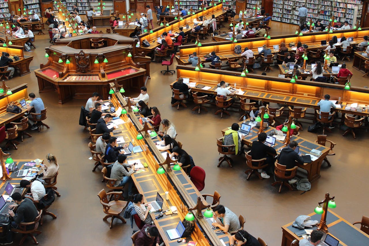 Een grote bibliotheek met veel mensen die aan bureaus zitten en werken achter hun laptop.