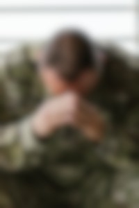 Een soldaat in een camouflage-uniform met zijn handen op zijn gezicht.
