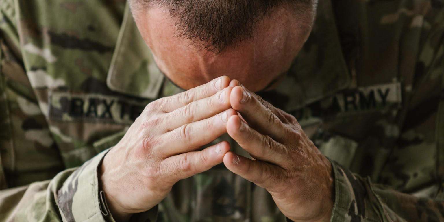 Een soldaat in een camouflage-uniform met zijn handen op zijn gezicht.