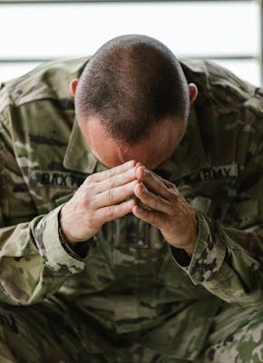 Een soldaat in een camouflage-uniform met zijn handen op zijn gezicht.