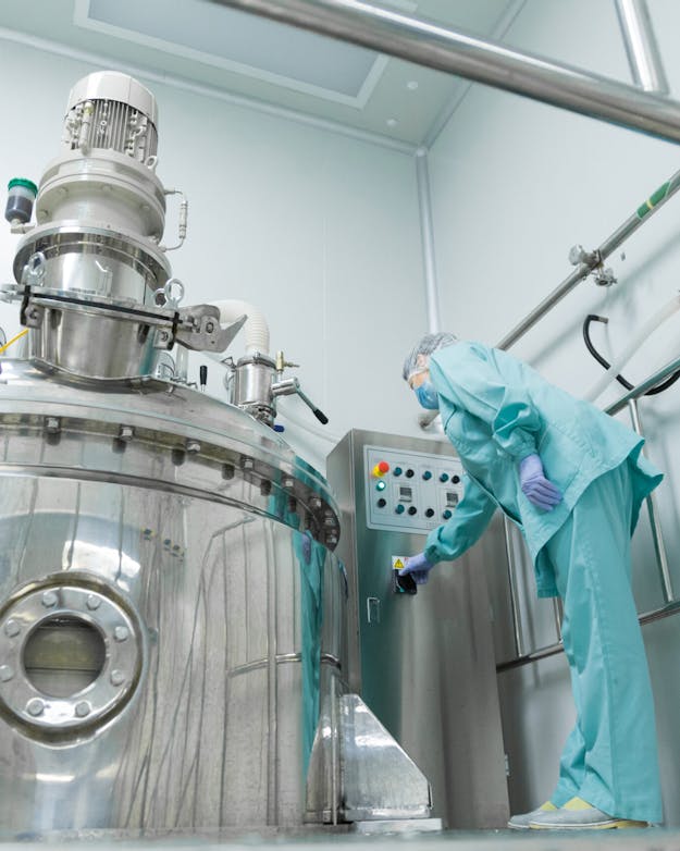 In grote kweekreactoren maken aangepaste losse cellen de eiwitten van de toekomst. Het krijgt vaak de naam precisiefermentatie, maar microbiologen zijn kritisch op die naam. Het is meestal geen fermentatie, dat is namelijk een proces in afwezigheid van zuurstof, terwijl juist eiwitten maken beter gaat met gebruik van zuurstof. Groot rvs reactorvat met ernaast een vrouw in beschermende kleding.