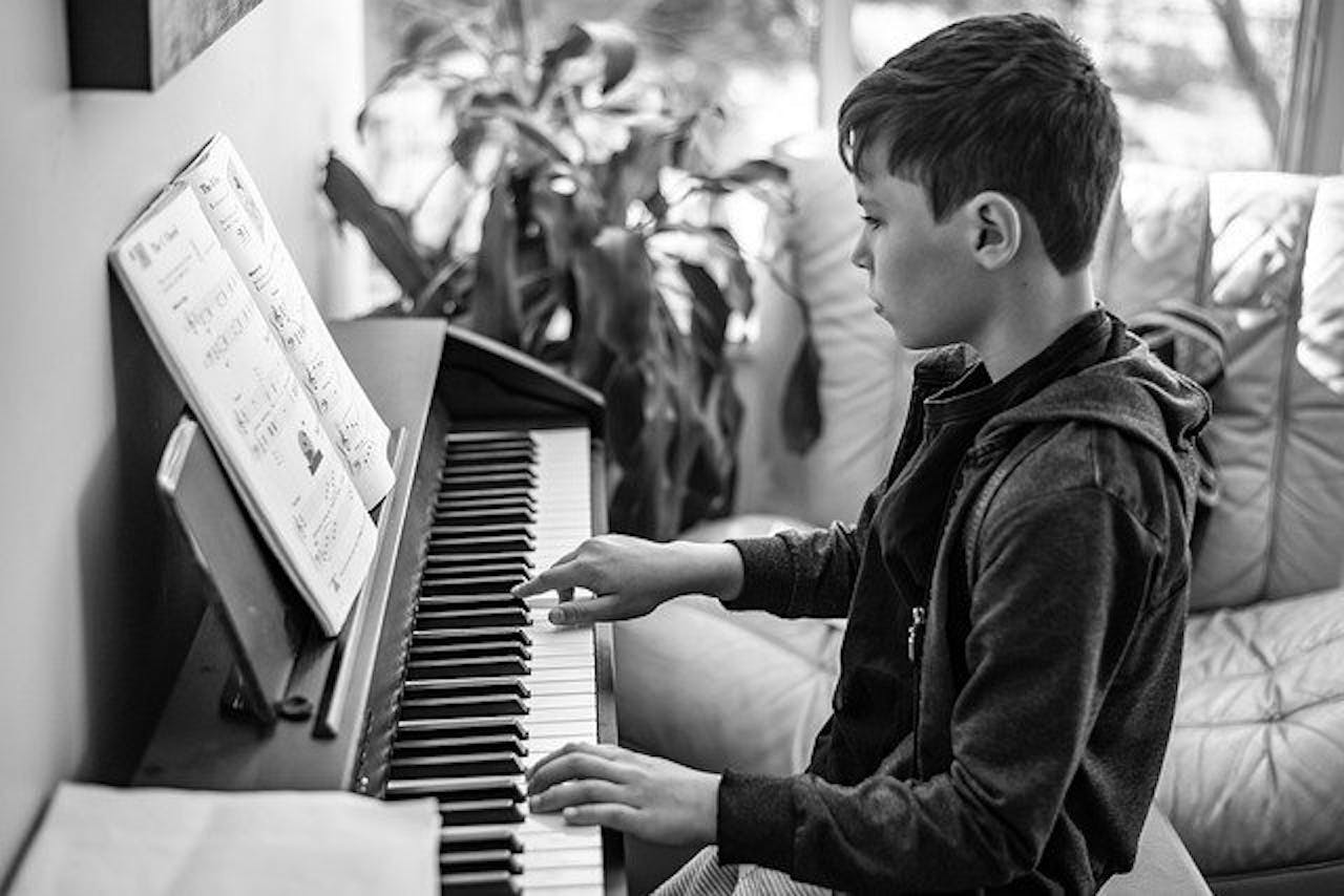 Een zwart-witfoto van een jongen die piano speelt.