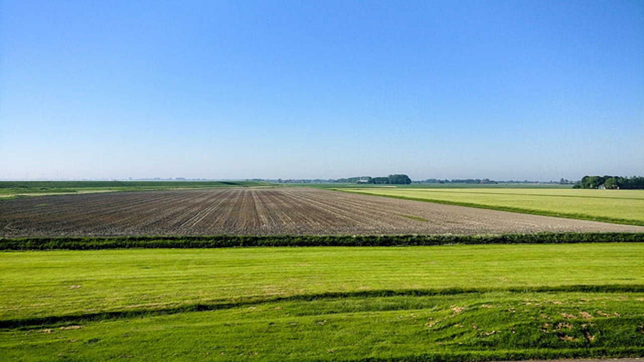 Een vlak landschap met een akker en grasvelden.