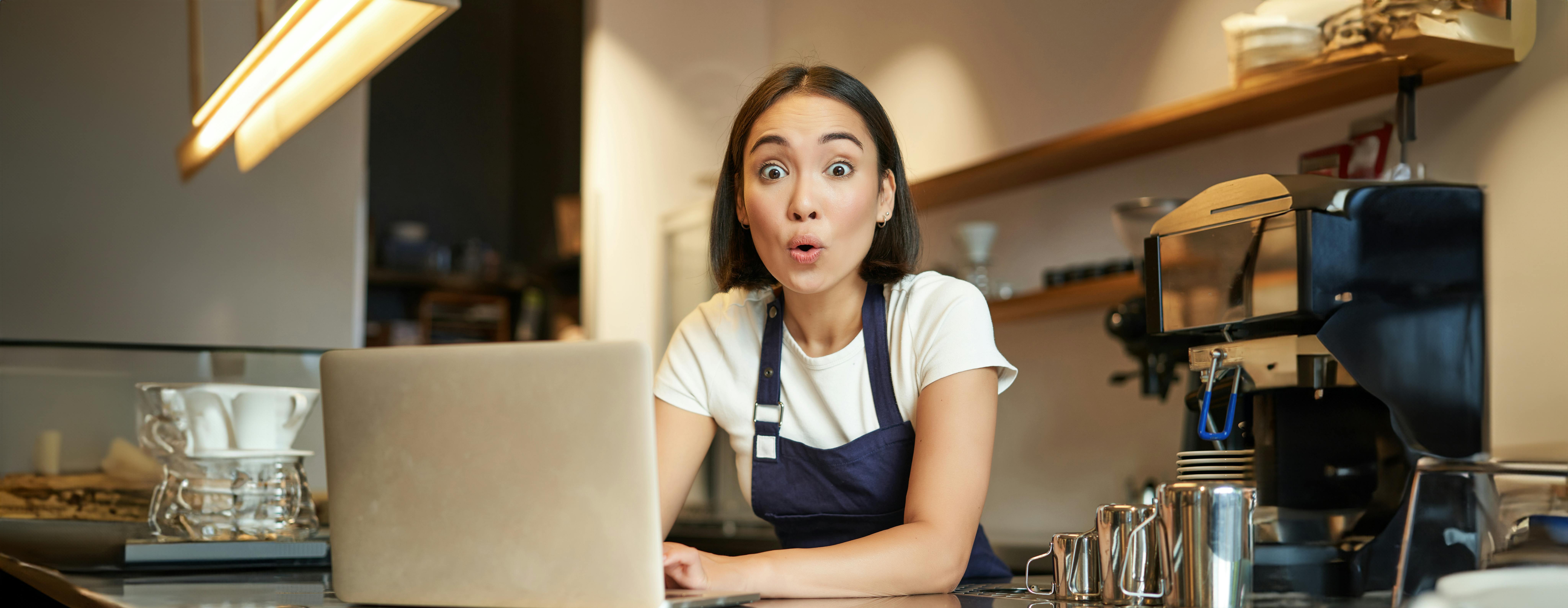 Een vrouw kijkt verschrikt op met een laptop voor haar gezicht