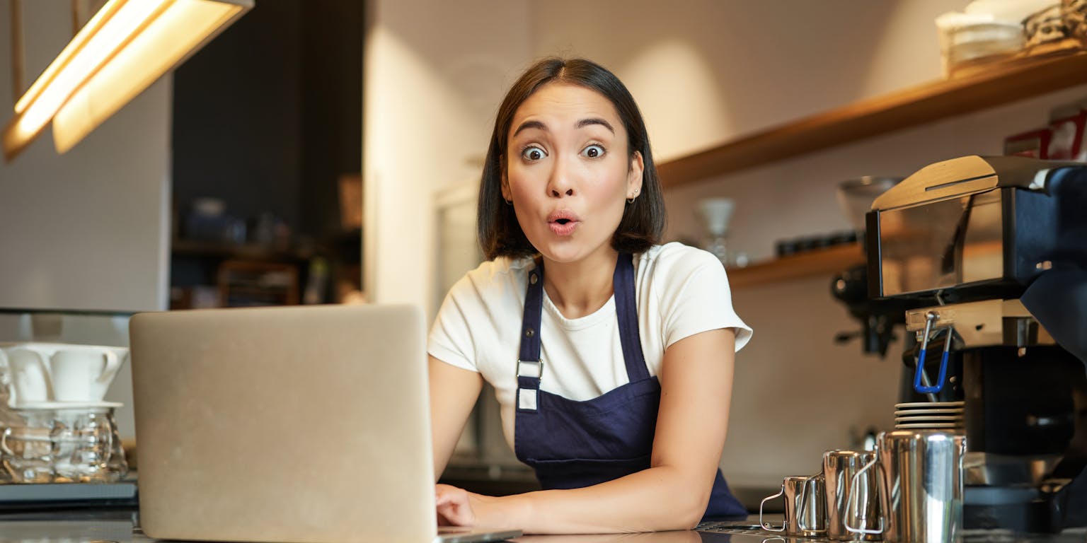 Een vrouw kijkt verschrikt op met een laptop voor haar gezicht