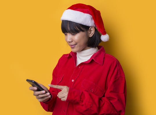 tienermeisje met kerstmuts op en gele achtergrond kijkt op mobiel