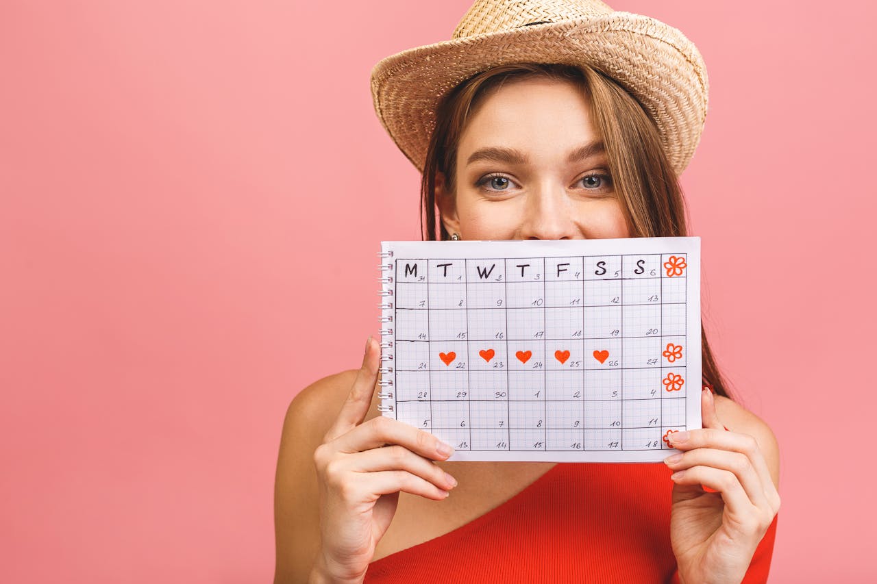 jonge vrouw verstopt zich achter kalender, op de kalender is te zien wanneer zij menstrueert