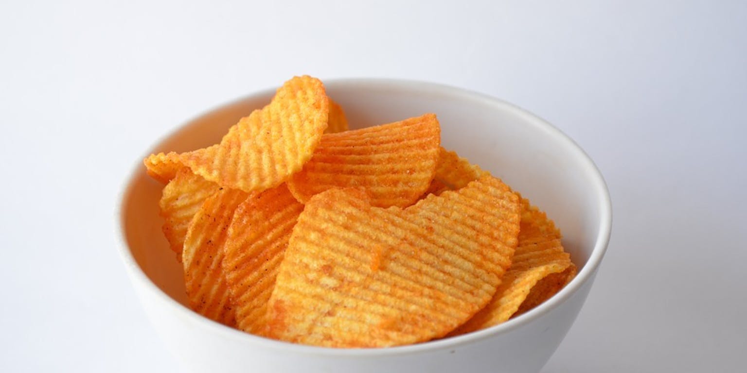 Aardappelchips in een witte kom op een witte achtergrond.