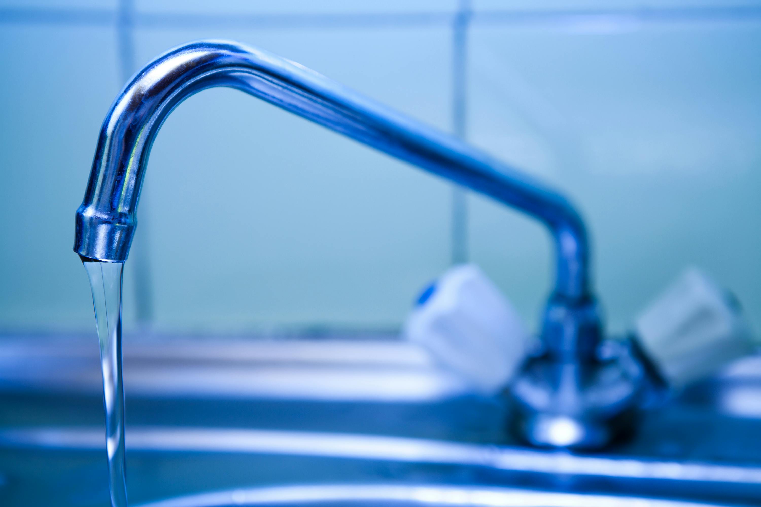 Close-up van een kraan waar een straal water uit loopt.