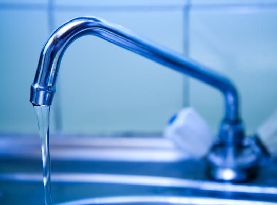 Close-up van een kraan waar een straal water uit loopt.