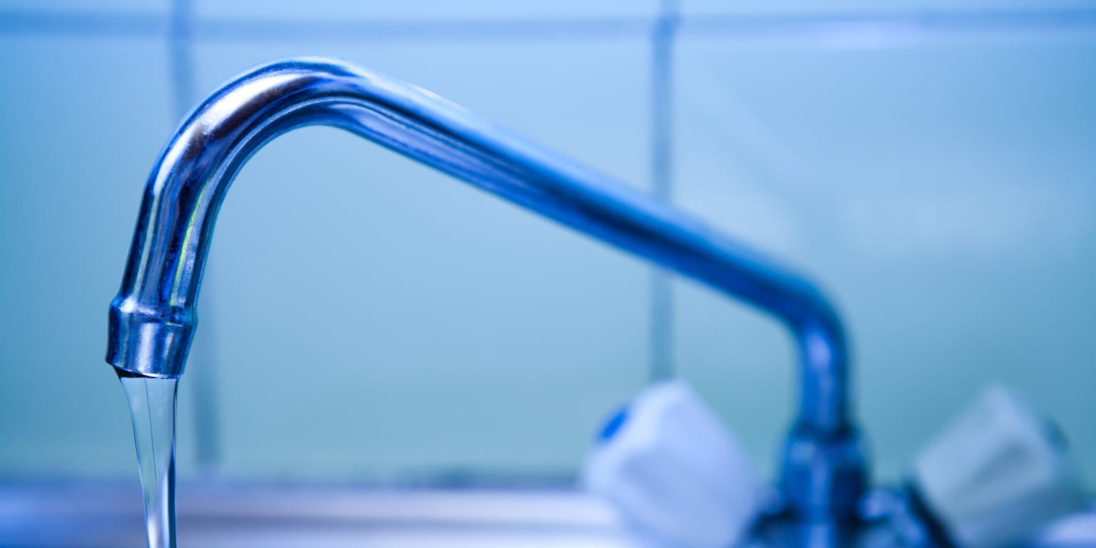 Close-up van een kraan waar een straal water uit loopt.