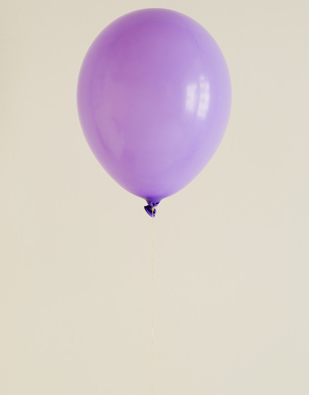 Opgeblazen paarse ballon met een fijn touwtje eraan tegen een beige achtergrond.