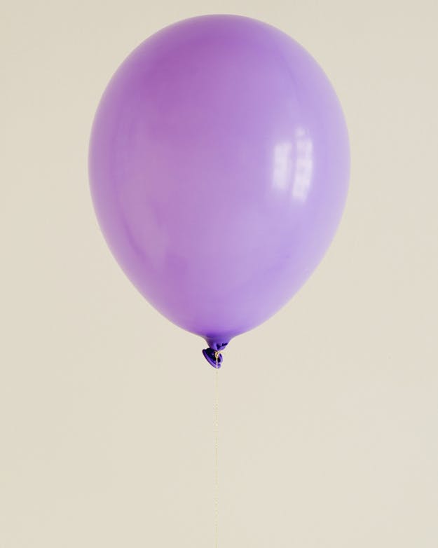 Opgeblazen paarse ballon met een fijn touwtje eraan tegen een beige achtergrond. Opgeblazen paarse ballon met een fijn touwtje eraan tegen een beige achtergrond.