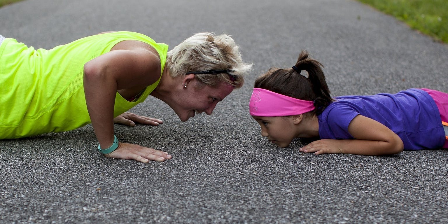 Een vrouw en een klein meisje doen push-ups op een weg.