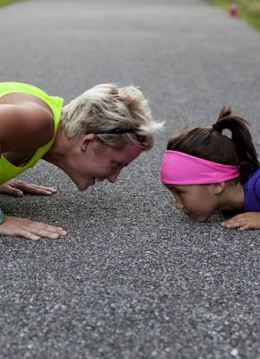 Een vrouw en een klein meisje doen push-ups op een weg.