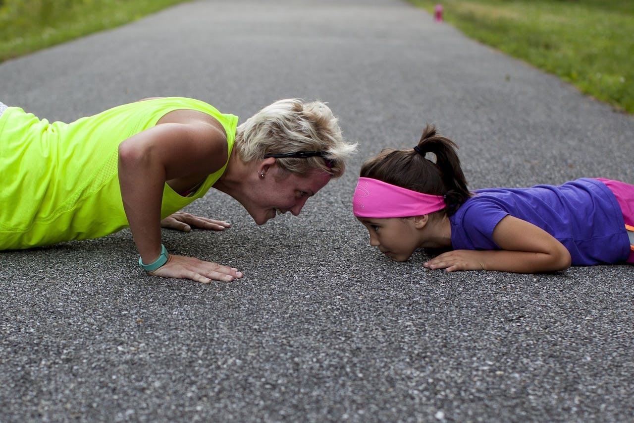 Een vrouw en een klein meisje doen push-ups op een weg.