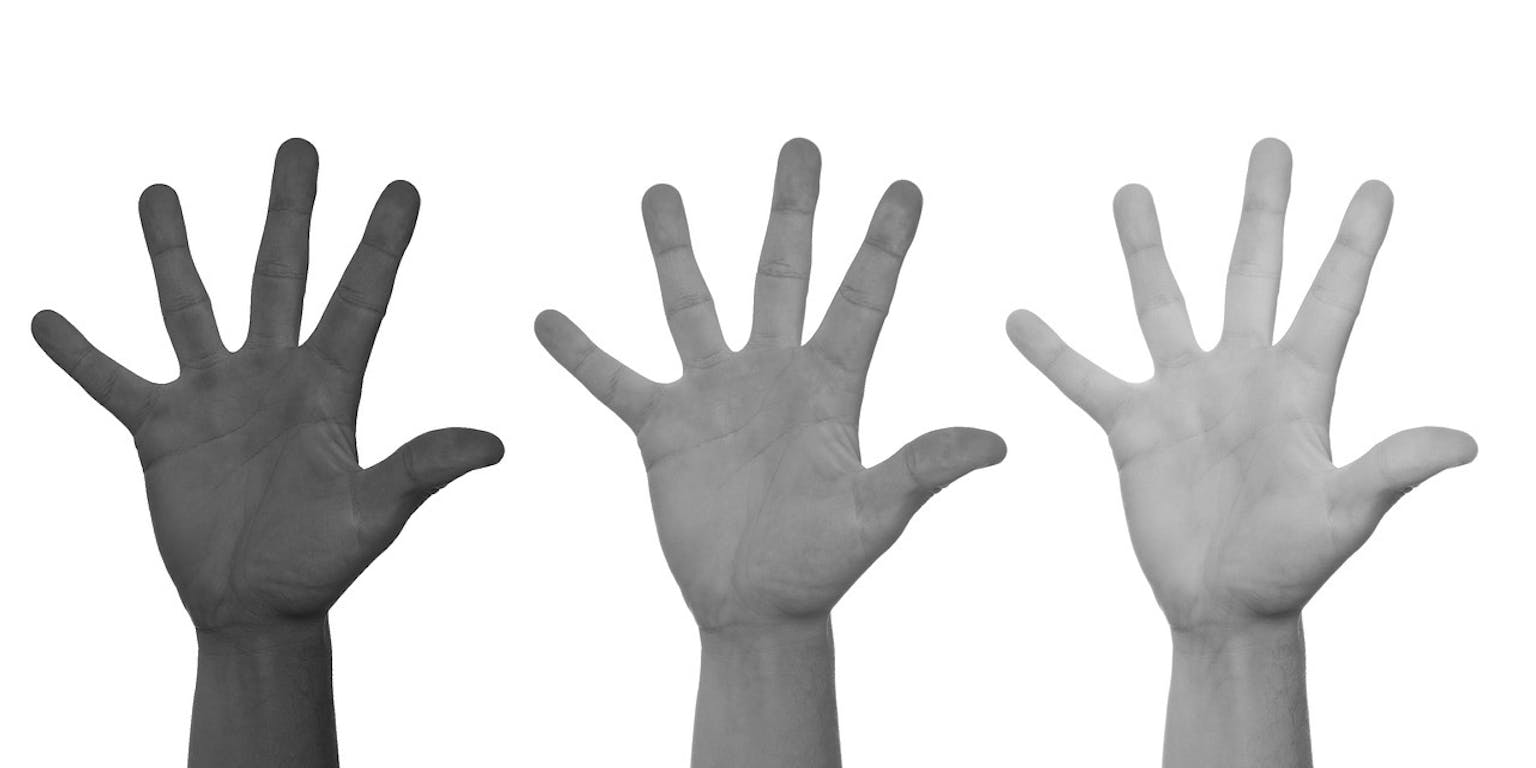 Een zwart-witfoto van drie handen in verschillende huidskleuren.