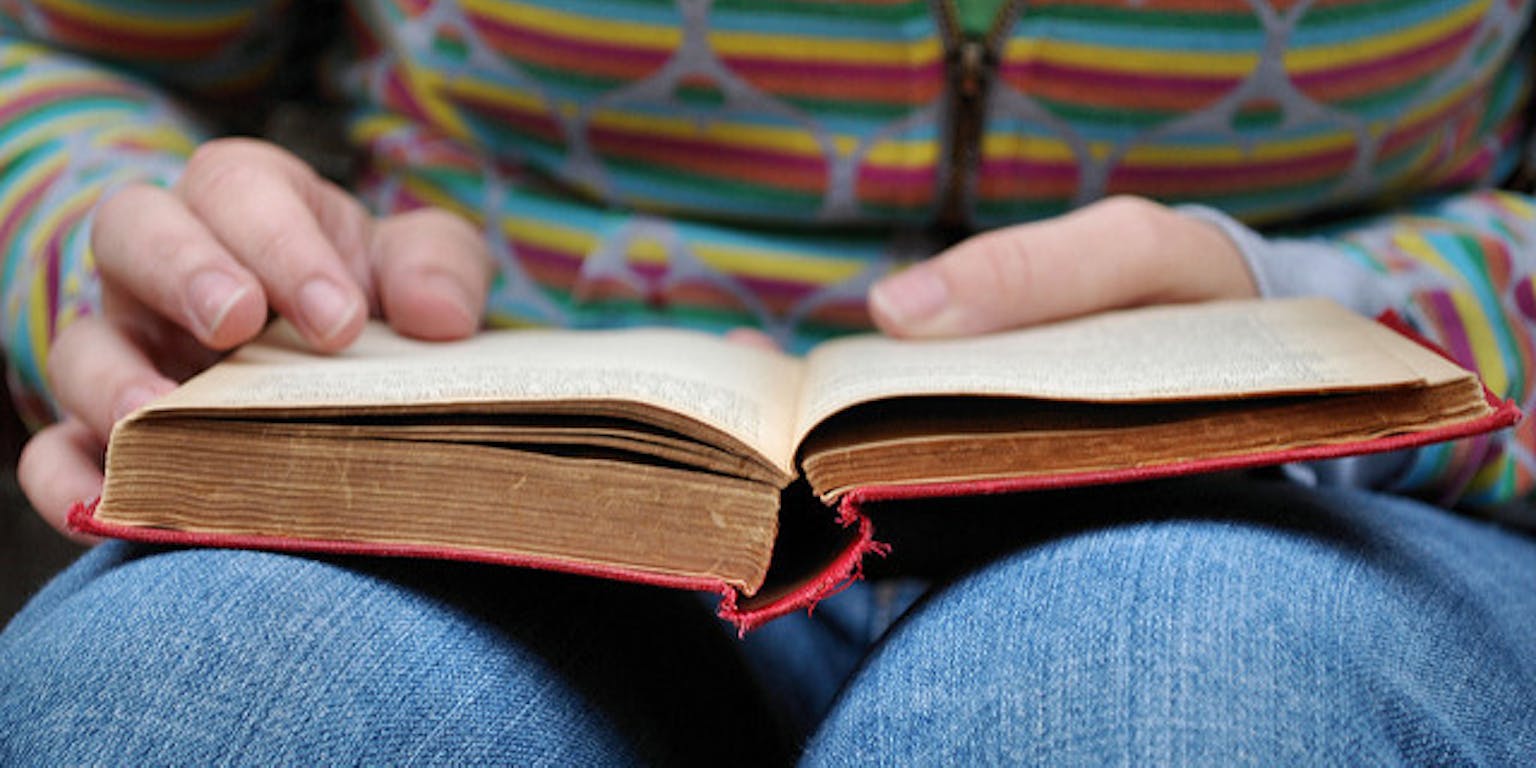 Een persoon leest een boek die op schoot ligt.
