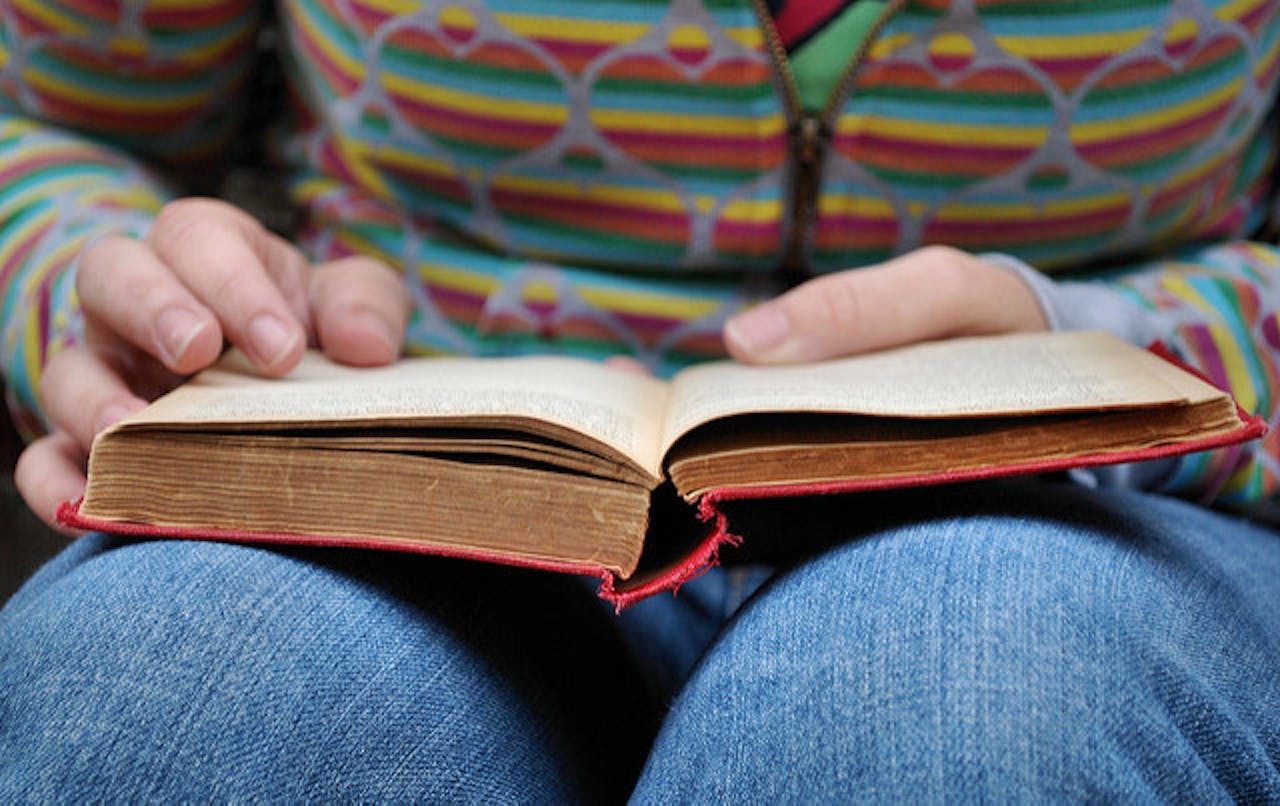 Een persoon leest een boek die op schoot ligt.