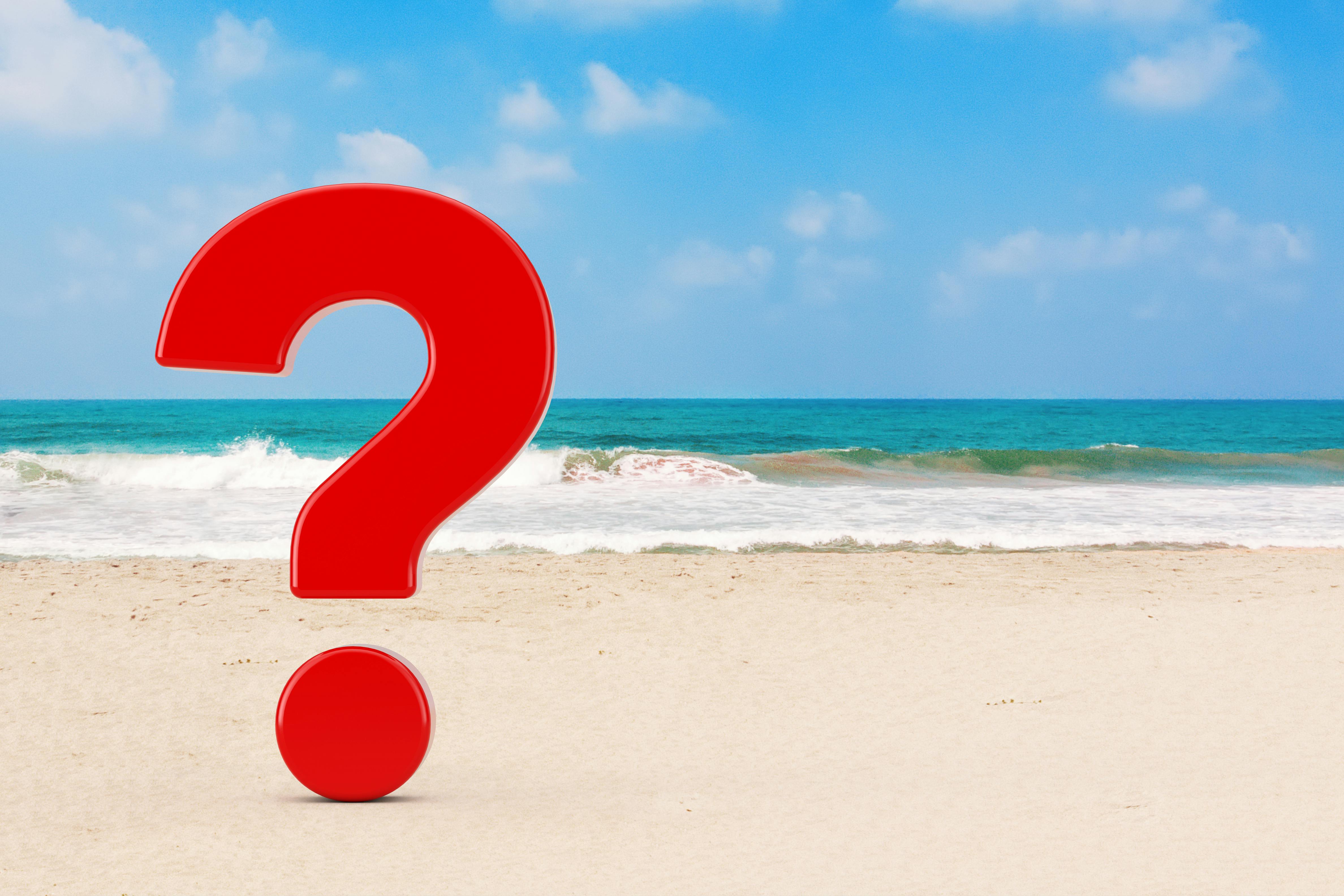 een rood vraagteken op het strand met zee op de achtergrond