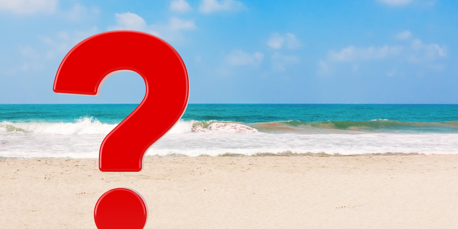 een rood vraagteken op het strand met zee op de achtergrond