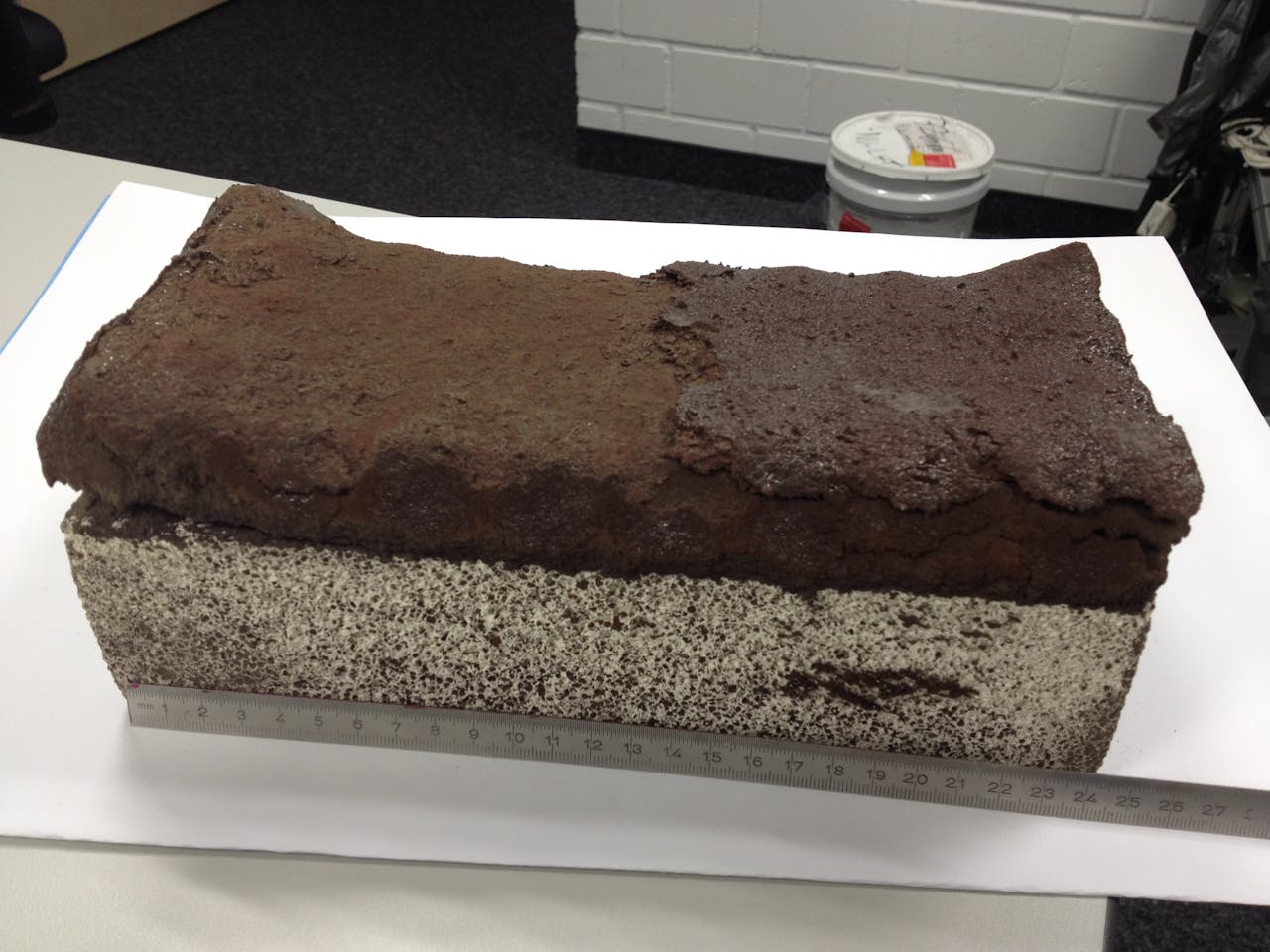 Een 24 centimeter lange baksteen van replica-regoliet, uit de 3D-printer. In donkerbruin de geprinte steen (het grijze blok eronder dient als ondersteuning).