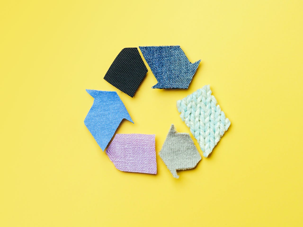 recycleteken gemaakt met stukjes stof in verschillende kleuren op een gele achtergrond