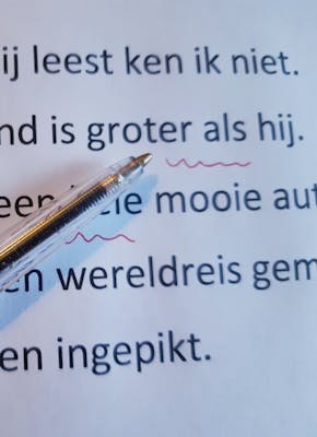 Op een vel papier ligt een rode pen waarmee fouten in de tekst zijn onderstreept.