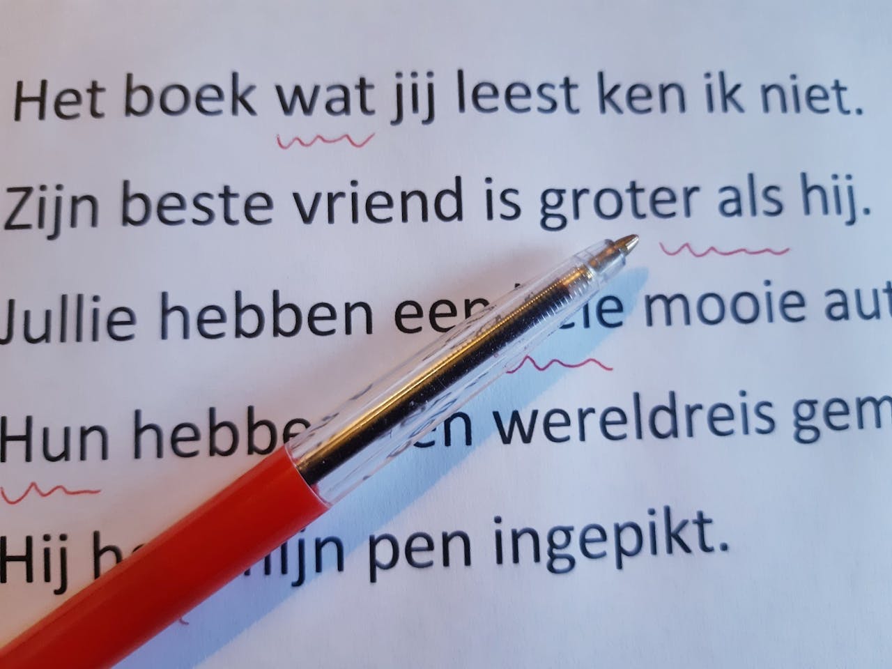 Op een vel papier ligt een rode pen waarmee fouten in de tekst zijn onderstreept.