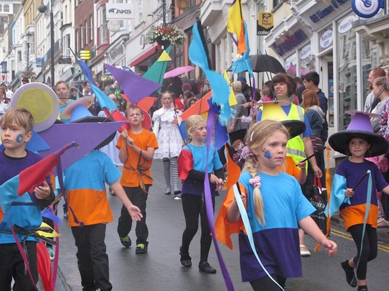 Een groep kinderen gekleed in kleurrijke kostuums loopt door de straat.
