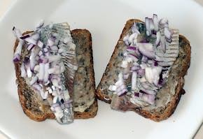 Twee sneetjes brood met haring en uitjes erop.